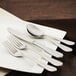 A white plate with a Walco Goddess stainless steel bouillon spoon on it.