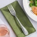 A Libbey stainless steel dinner fork on a green napkin next to a plate of food.