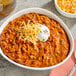 A bowl of Vanee chili without beans with cheese and sour cream on a table in a family-style restaurant.