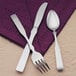 A Libbey stainless steel demitasse spoon on a purple napkin.