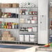 A Regency stainless steel wire shelving unit in a large kitchen with food items and containers on the shelves.