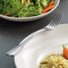 A Libbey stainless steel dessert fork next to a plate of rice and vegetables.