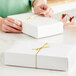 A person tying a yellow ribbon on a white candy box.