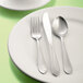 A Libbey stainless steel medium weight dessert spoon on a white plate.