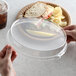 A person holding a Solut clear plastic lid over a plate of food.