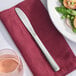 A Libbey Windsor stainless steel dinner knife on a red napkin next to a plate of food.