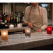 A group of Sterno smoke votive liquid candle holders on a marble counter with lit red candles.