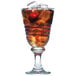 A glass of brown liquid with ice and a cherry on top.