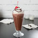 A glass of Ghirardelli Sweet Ground Dark Chocolate cocoa with whipped cream and a cherry.