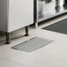 A rectangular 12" x 24" stainless steel floor trough with a grate, installed in a tiled floor.