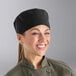 A woman wearing a Mercer Culinary black chef's skull cap.