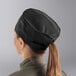 A woman wearing a black Mercer Culinary baker's skull cap with a ponytail.