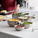 A woman using Vollrath stainless steel mixing bowls to prepare a variety of foods.