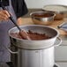 A person stirring chocolate in a Vollrath stainless steel mixing bowl.