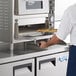 A man using an Avantco countertop pizza oven to bake a pizza on a cordierite pizza stone.