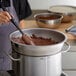 A person stirring chocolate in a stainless steel bowl.