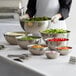 A woman preparing a salad in a large stainless steel mixing bowl.