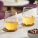 Two Arcoroc Perfection stemless wine glasses filled with yellow liquid on a marble counter.