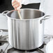 A person stirring a large silver stock pot with a wooden spoon.