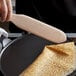 A person using the Fox Run beechwood crepe spatula to cook a crepe in a frying pan.