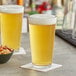 Two Acopa mixing glasses of beer on a bar counter.