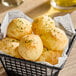 A basket of round, golden-brown cheese bread rolls garnished with herbs, served on parchment paper.