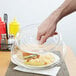 A hand using a Carlisle clear plate cover to take a sandwich from a salad bar.