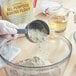 A gloved hand pours Bob's Red Mill gluten-free flour into a bowl.