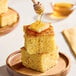 A stack of cornbread squares topped with butter and honey on a wooden plate.