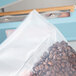 A person using an Omcan manual impulse bag sealer to seal a bag of coffee beans.