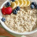 A bowl of oatmeal topped with sliced bananas, blueberries, and a strawberry.