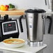 A silver and black AvaMix stainless steel blender next to a white bowl of brown liquid.