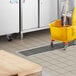 A yellow mop and bucket in a kitchen with a white rectangular floor trough.