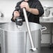 A man using a Waring immersion blender shaft in a large pot.