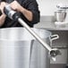 A man using a Waring immersion blender in a large metal container.