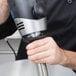 A hand using a Waring stainless steel shaft attachment on a black and silver immersion blender.