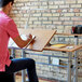 A man sitting at a Safco Medium Oak drafting table writing on a notebook.