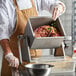 A person in a white coat and apron using a Backyard Pro manual tilting meat mixer to prepare meat.