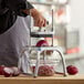 A person using a Vollrath push block to slice a red onion on a table.