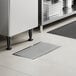 A rectangular 12" x 24" stainless steel floor water receptacle with a grate, installed in a tiled floor.