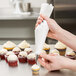 A person decorating a cupcake with a white Ateco polyurethane coated pastry bag.