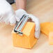 A person in gloves uses a Thunder Group Aluminum cheese slicer to cut cheese on a counter.