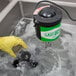 A hand in a yellow glove using a Noble Products glass washer brush to clean a glass jar.