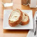 A white Acopa square porcelain plate with a piece of bread and butter on it.