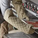 A person in a brown apron using SafeMitt oven mitts to hold a tray of meat.