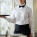 A woman holding a tray with wine glasses wearing a white tuxedo shirt with a wing tip collar.