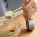 A person using a Vollrath stainless steel measuring spoon to measure green powder.