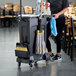 A woman using a mop from a cleaning cart to clean a table in a restaurant.