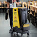 A person standing next to a Rubbermaid Slim Jim trash cart with cleaning supplies.