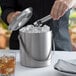 A woman using tongs to put ice in a Franmara stainless steel ice bucket.